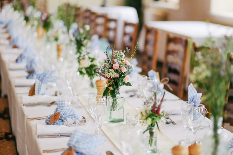 Long reception table dressed with wildflowers in glass jars and blue gingham napkins
