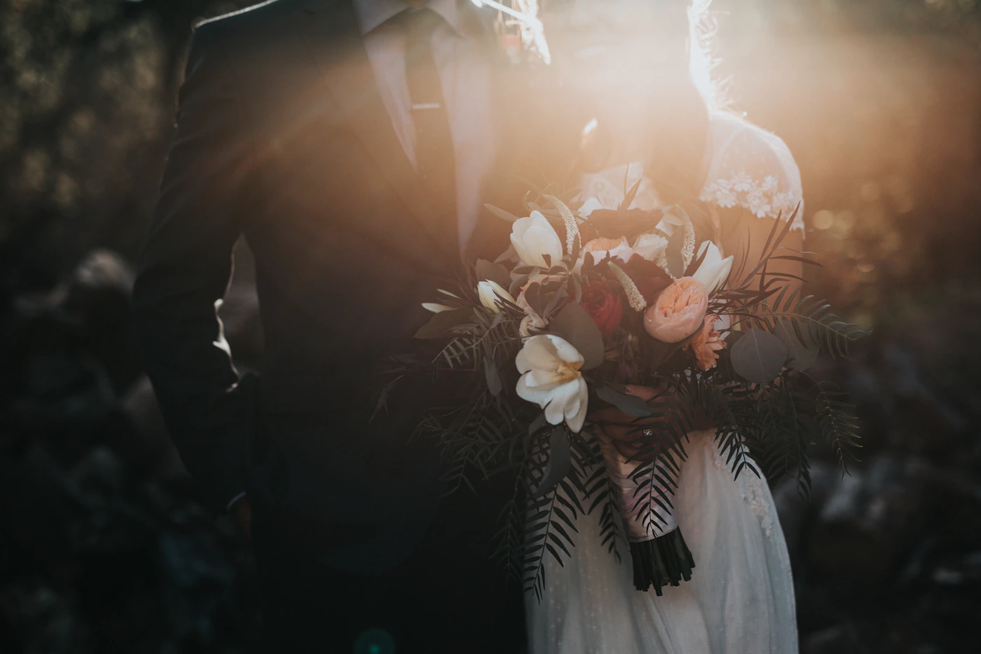 Couple backlit at golden hour, the bridal bouquet catching the last of the sun