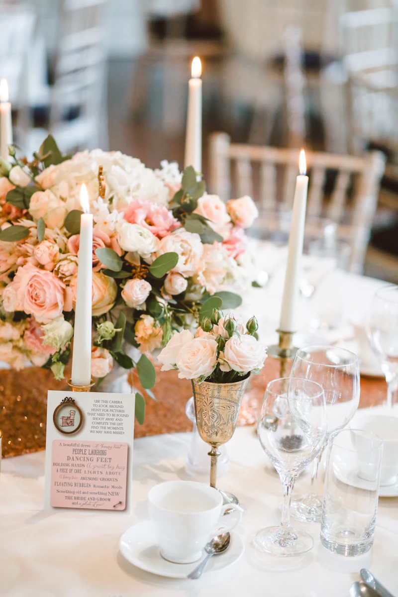 Reception centerpiece of blush roses with lit taper candles, a gold goblet and a place setting