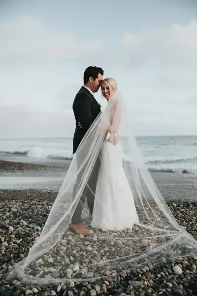 Noa and Eli at the water's edge, the bride's long veil sweeping across the beach
